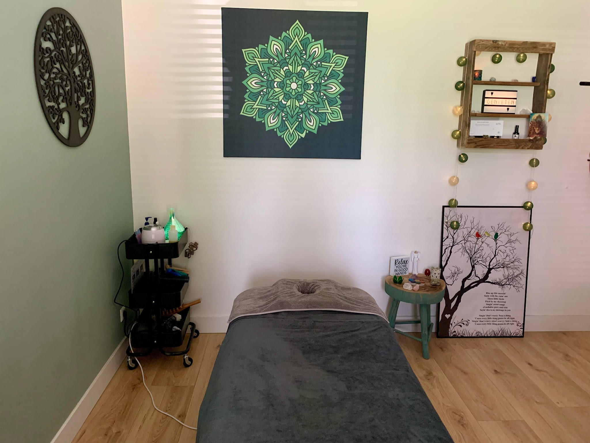 De behandelkamer: massagetafel met grijs linnen, een groen mandaladoek en planten