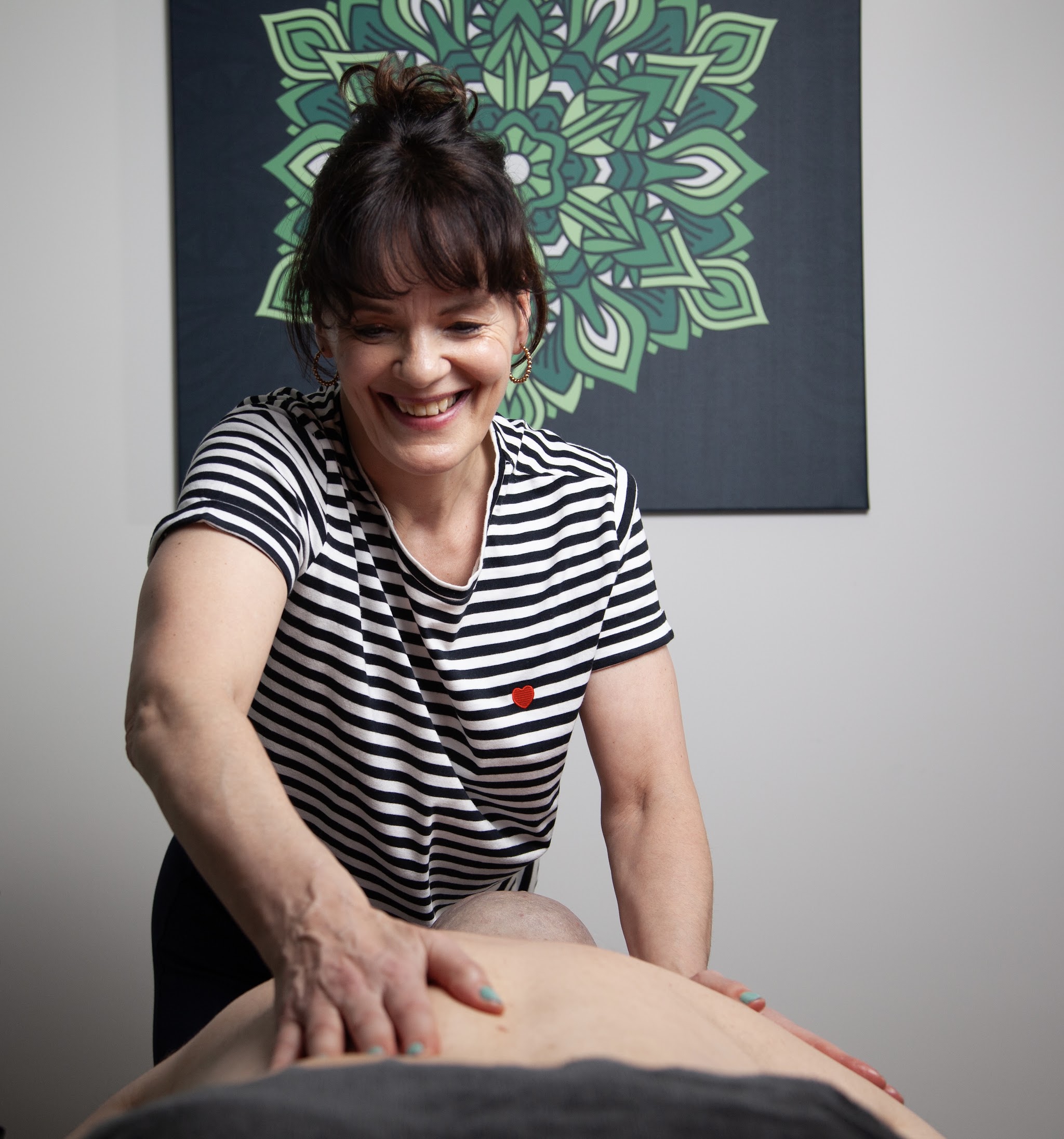 Adriënne lacht terwijl ze de rug van een cliënt masseert, met het groene mandaladoek achter haar