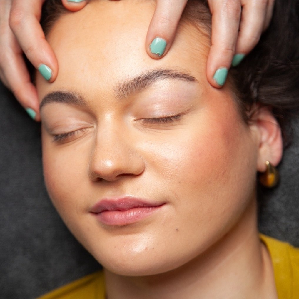 Voorhoofdmassage, de cliënt glimlacht met gesloten ogen